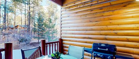 A wooden cabin with a round table and chairs, a grill, and a potted plant.