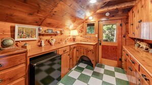 Une cuisine chaleureuse, aménagée dans le style d’un chalet, avec des meubles en bois, un carrelage à carreaux et un petit évier.