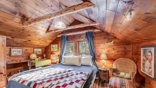 Une chambre confortable dans un chalet en rondins, avec un grand lit, un fauteuil en osier et un globe terrestre posé sur une table d’appoint.