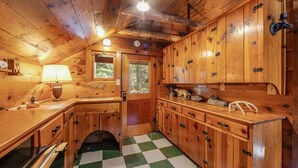 L’intérieur d’une cabane en bois, avec un plancher à carreaux, des armoires en bois, un évier et une fenêtre donnant sur les arbres.