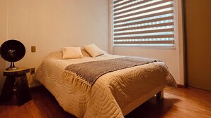Ein Schlafzimmer mit einem Bett, einer Nachttischlampe, einem Fenster mit Jalousien und einer Tür.