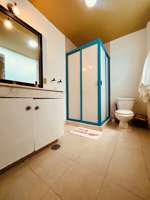 Ein Badezimmer mit weißem Waschtisch, einem Spiegel, einer Toilette und einer Duschkabine.