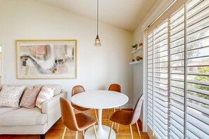 A dining area with a round white table and brown chairs, a hanging pendant light, and a large abstract painting on the wall. - Palm Desert Resorter | New Furnishings | 20 Pools, Championship Golf (Palm Desert)