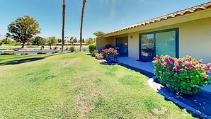 A modern house with a tiled roof, large windows, and a well-maintained lawn with pink flowers. - Palm Desert Resorter | New Furnishings | 20 Pools, Championship Golf (Palm Desert)