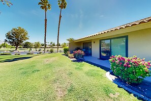 A modern house with a tiled roof, large windows, and a well-maintained lawn with pink flowers. - Palm Desert Resorter | New Furnishings | 20 Pools, Championship Golf (Palm Desert)