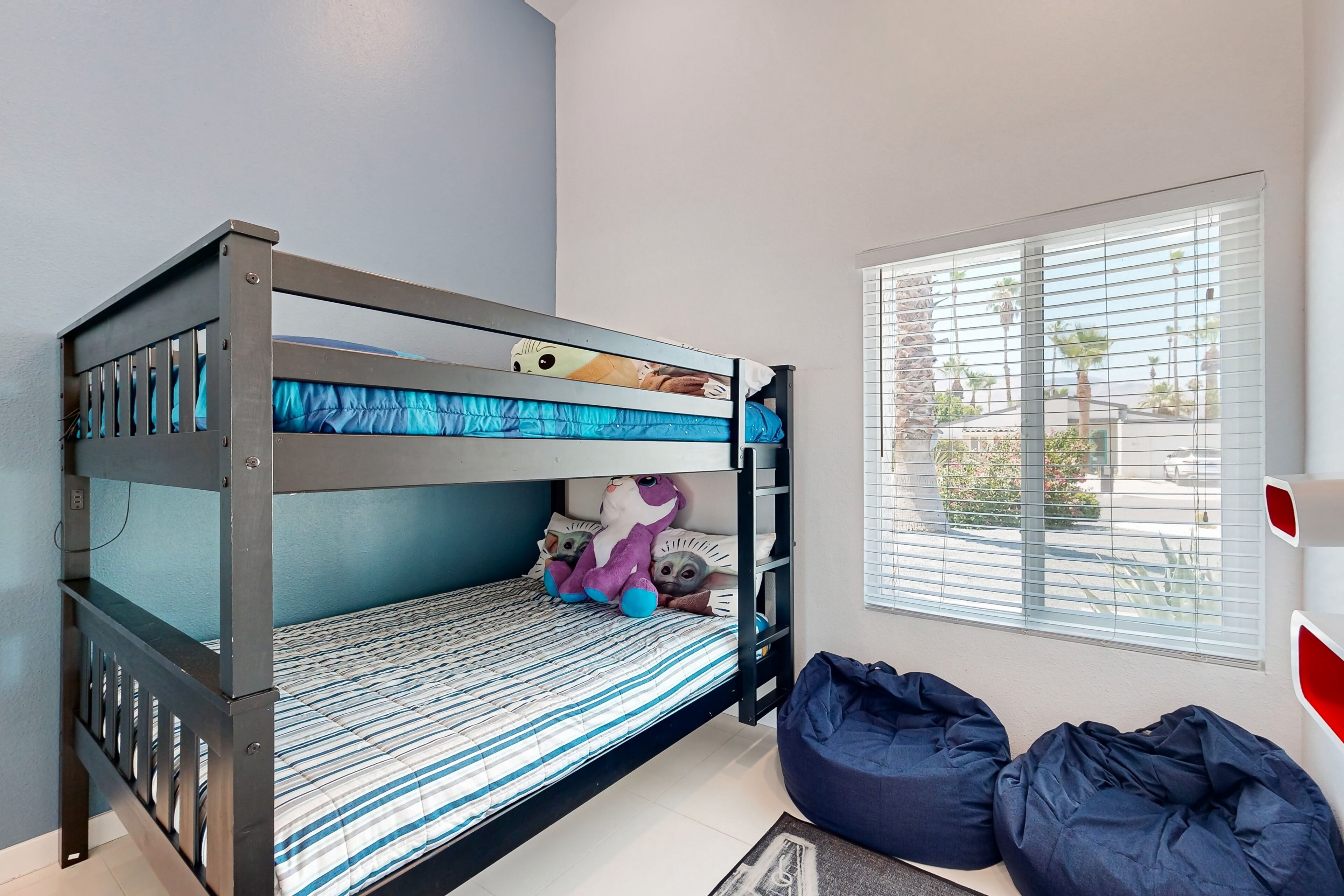 A bunk bed with a striped mattress, a window with blinds, and two bean bags.