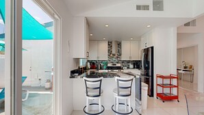 Una cocina moderna con armarios blancos, encimera negra y un carrito rojo.