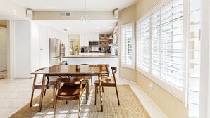 Une cuisine moderne avec des meubles blancs, un îlot central et un coin repas comprenant une table et des chaises en bois.