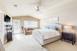 A bedroom with a large bed, a ceiling fan, a TV, a bookshelf, and a window. - Desert Delight | Corner Lot, Pool & Spa | Putting Greens & Hammock (Palm Desert)