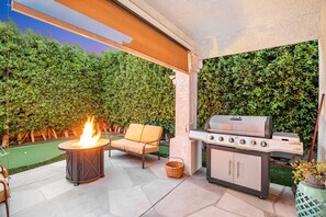 An outdoor patio with a fire pit, a grill, and a cushioned chair. - Desert Delight | Corner Lot, Pool & Spa | Putting Greens & Hammock (Palm Desert)
