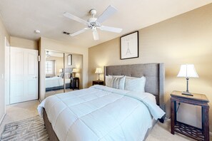 Une chambre avec un grand lit, un ventilateur de plafond, un tableau encadré représentant la Tour Eiffel et une table de chevet avec une lampe.