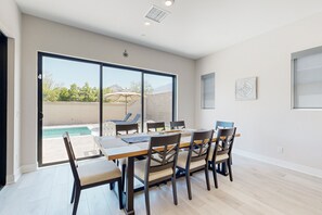 A dining area with a table and chairs, a view of a swimming pool, and a ceiling light fixture. - The Dream Weaver | House in La Quinta with a private pool and hot tub (La Quinta)