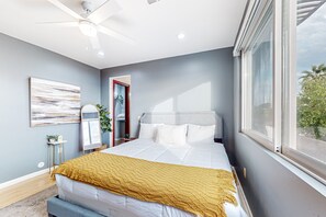 Ein Schlafzimmer mit Bett, Deckenventilator, Fenster und Blick ins Freie.
