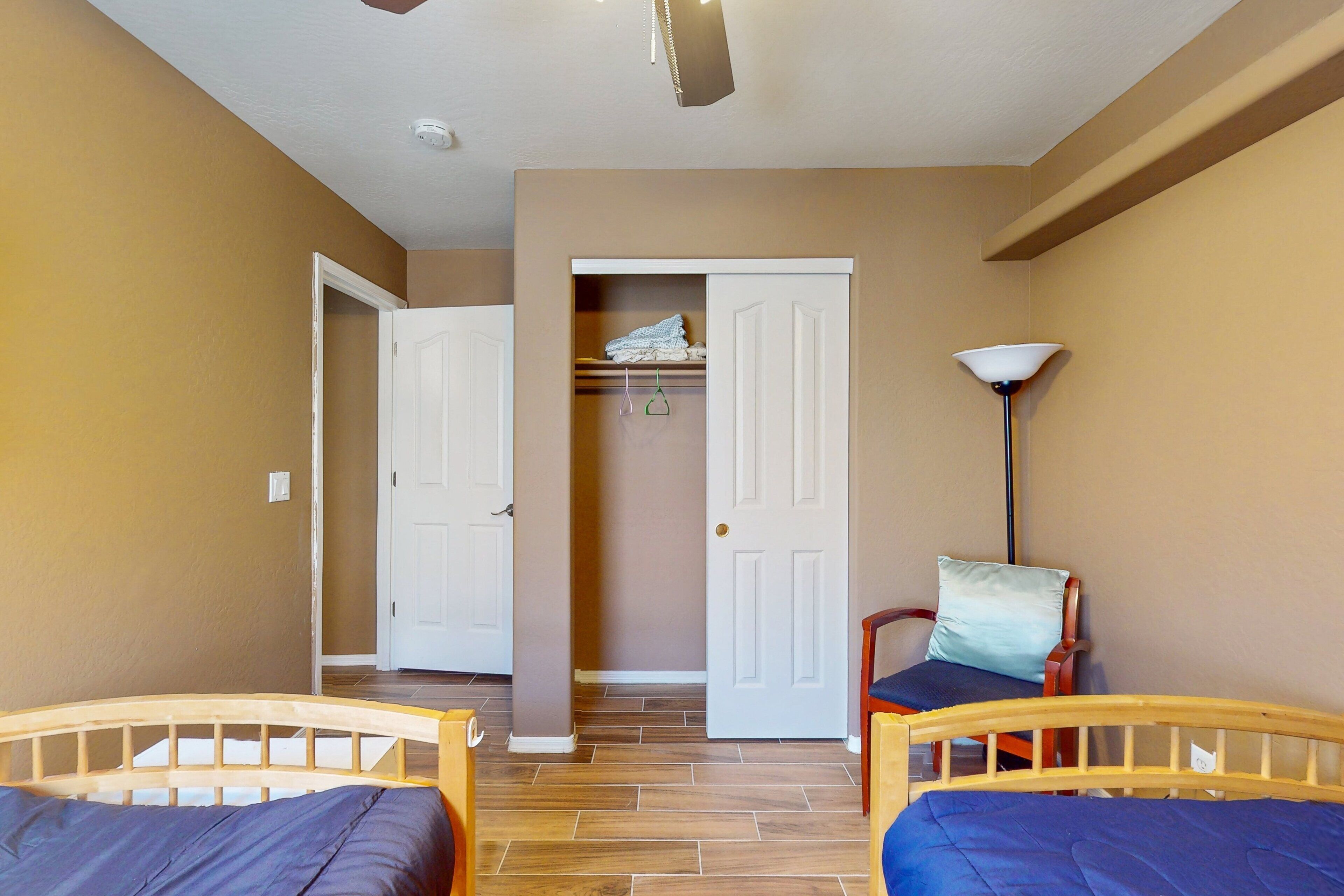 A room with two wooden beds, a closet with hanging clothes, and a floor lamp.
