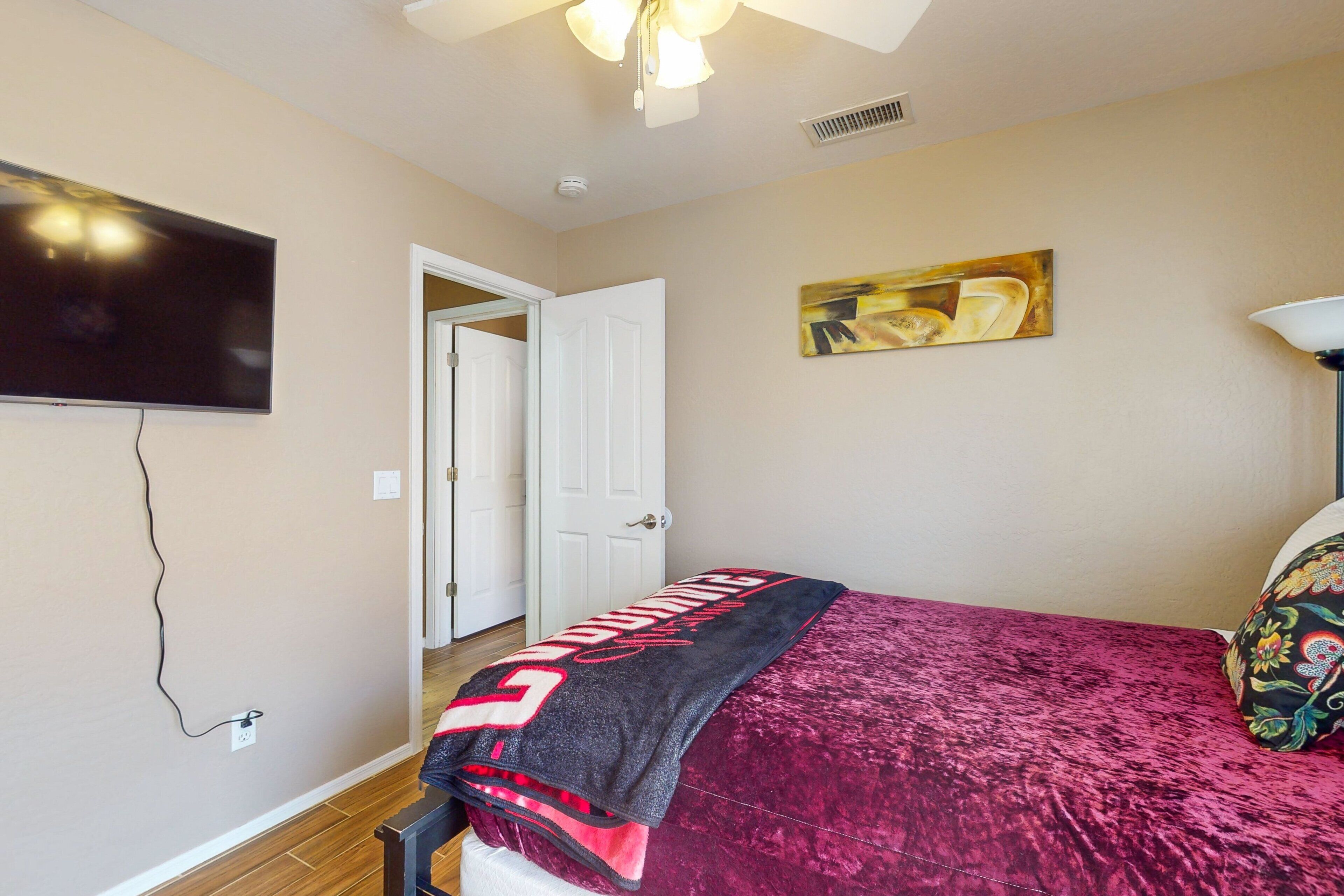 A bedroom with a bed, a television mounted on the wall, a door, and a painting.