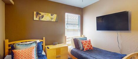 A bedroom with two beds, a nightstand, a wall-mounted TV, and a ceiling fan.