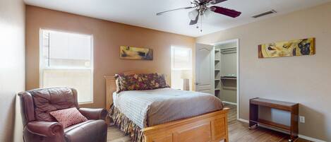 A bedroom with a wooden bed, a leather chair, a ceiling fan, and two windows.