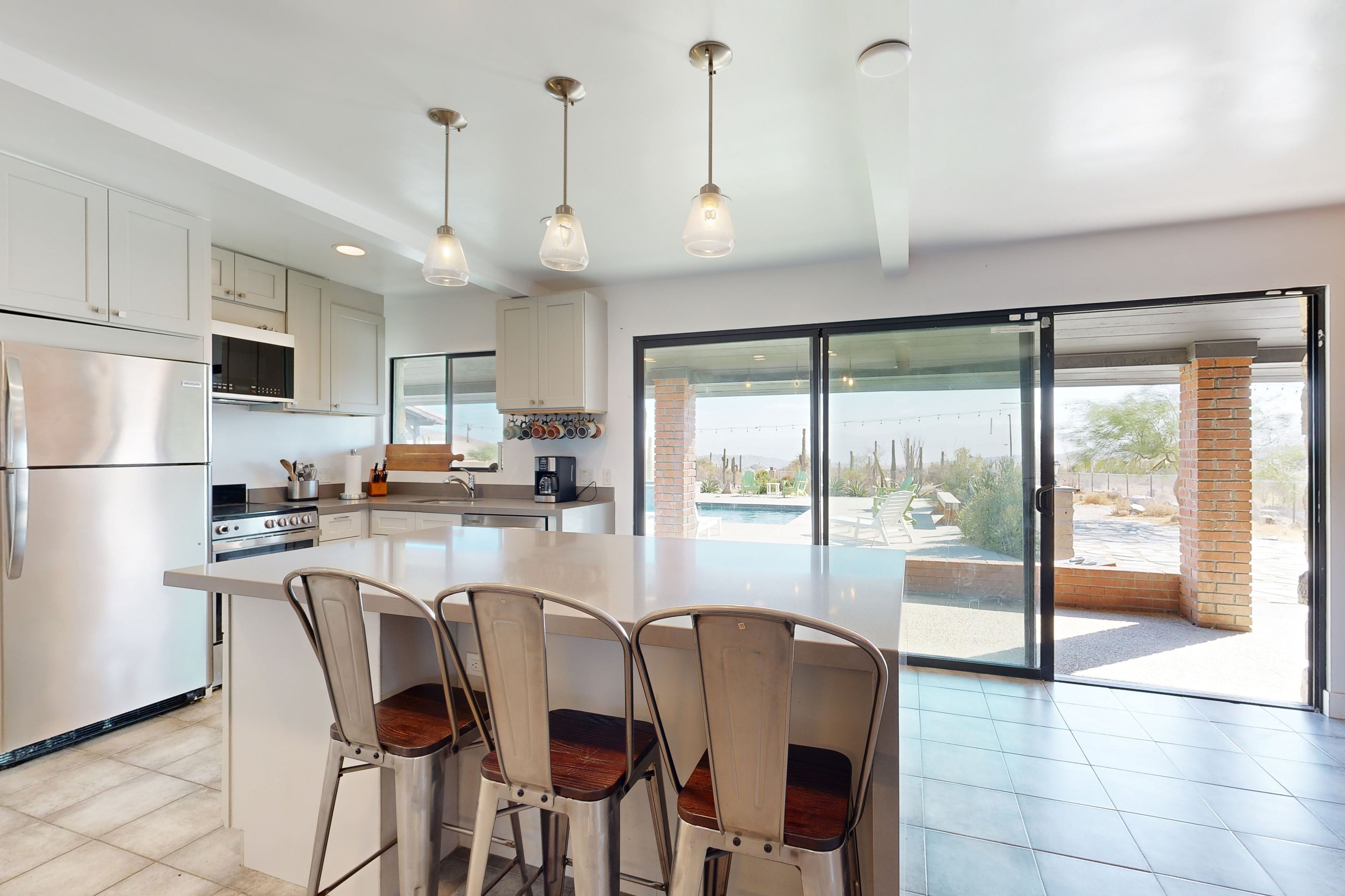 Een moderne keuken met witte kastjes, roestvrijstalen apparatuur en een groot eiland met barstoelen.