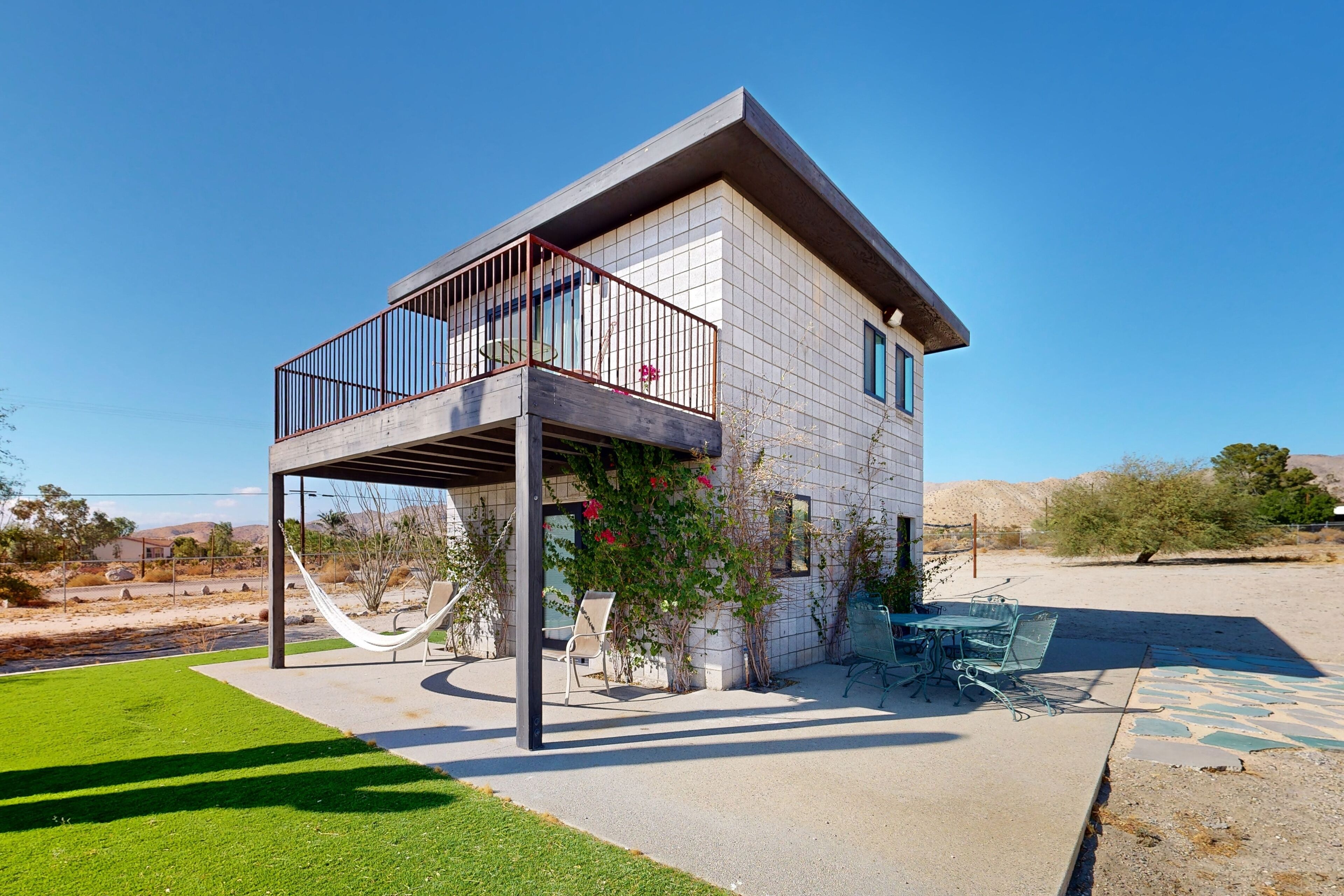 Una casa moderna con balcón, un patio con mobiliario exterior y un césped bien cuidado.