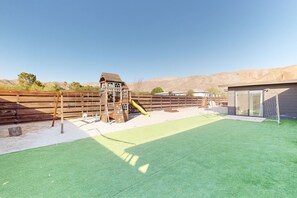 Ein eingezäunter Garten mit Spielplatz, Kunstrasen und einer Holzterrasse.