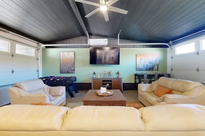 Eine geräumige Garage mit Deckenventilator, montiertem Fernseher und einer Sitzecke mit zwei Sofas und einem Couchtisch.