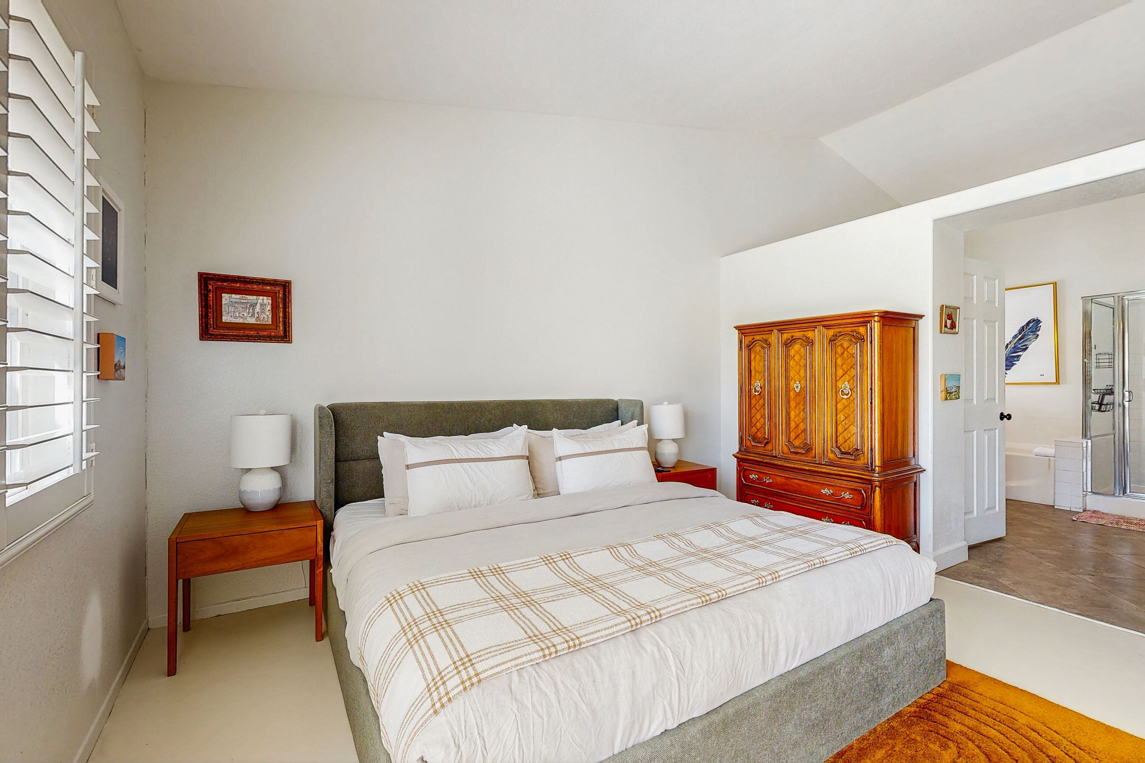 Une chambre à coucher avec un grand lit, une table de chevet en bois, une armoire et une fenêtre avec des stores.