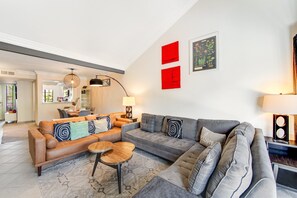 A modern living room with a sofa, coffee table, and a dining area in the background.