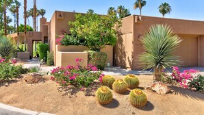 A desert-style building with a stucco exterior, palm trees, and cacti in the landscaping. - Cozy Dog-Friendly Condo, Shared Pool/Hot Tub, Near Golf Courses & National Park (Palm Desert)