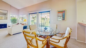 A modern living room with a glass-top dining table surrounded by wicker chairs, a white sofa, and a fireplace. - Cozy Dog-Friendly Condo, Shared Pool/Hot Tub, Near Golf Courses & National Park (Palm Desert)