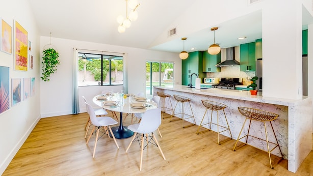A modern kitchen with a central island, bar stools, and a dining area with a round table and chairs. - Dog-friendly desert dream with a private pool, pool spa, & putting green (Palm Springs)