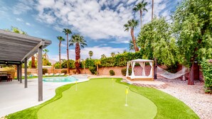 A backyard with a putting green, palm trees, a hammock, and a covered seating area. - Dog-friendly desert dream with a private pool, pool spa, & putting green (Palm Springs)