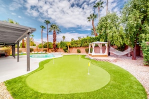 Ein Garten mit Putting-Grün, Palmen, einer Hängematte und einer überdachten Sitzgelegenheit.