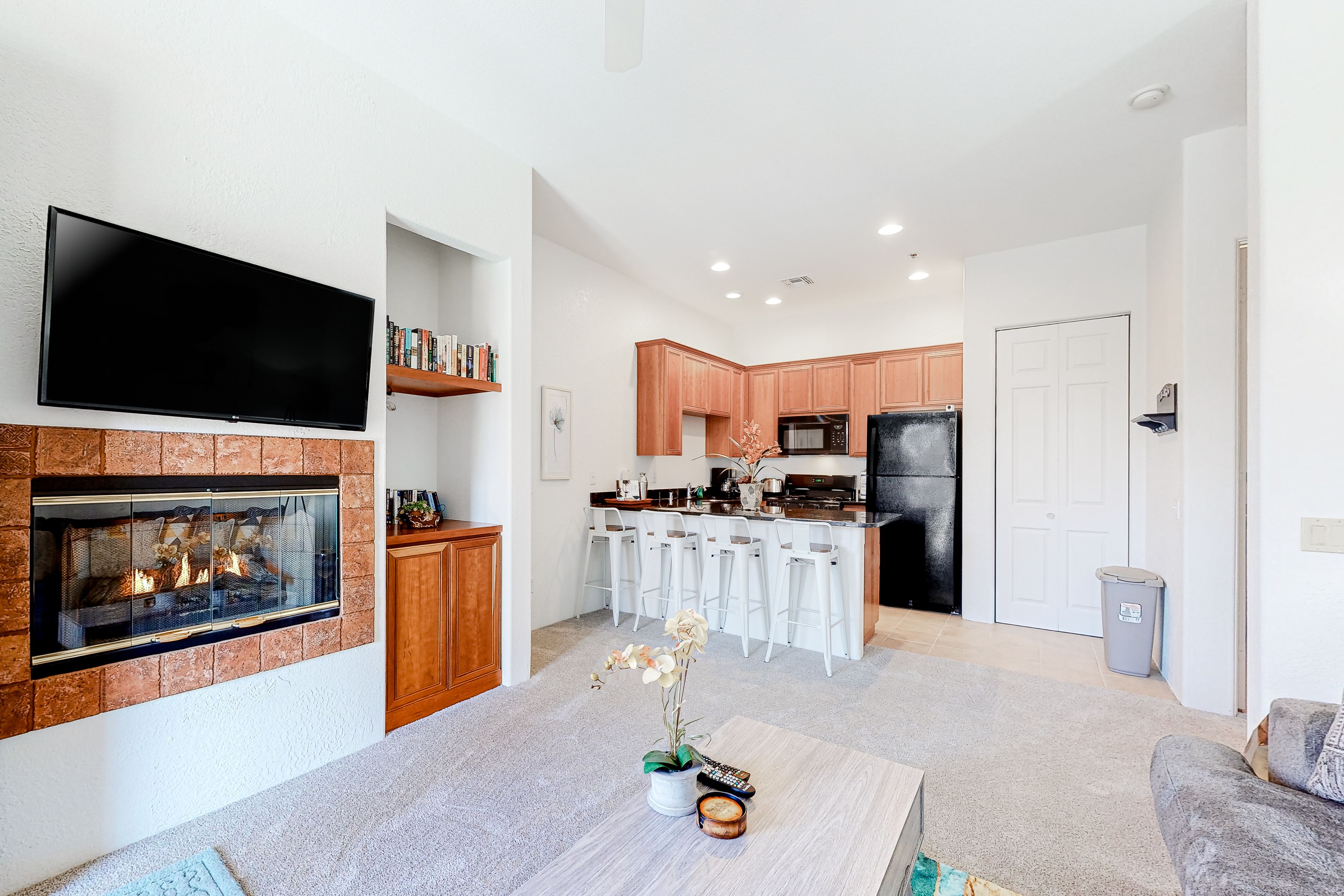 A modern living room with a fireplace, a flat-screen TV, and a kitchen in the background.