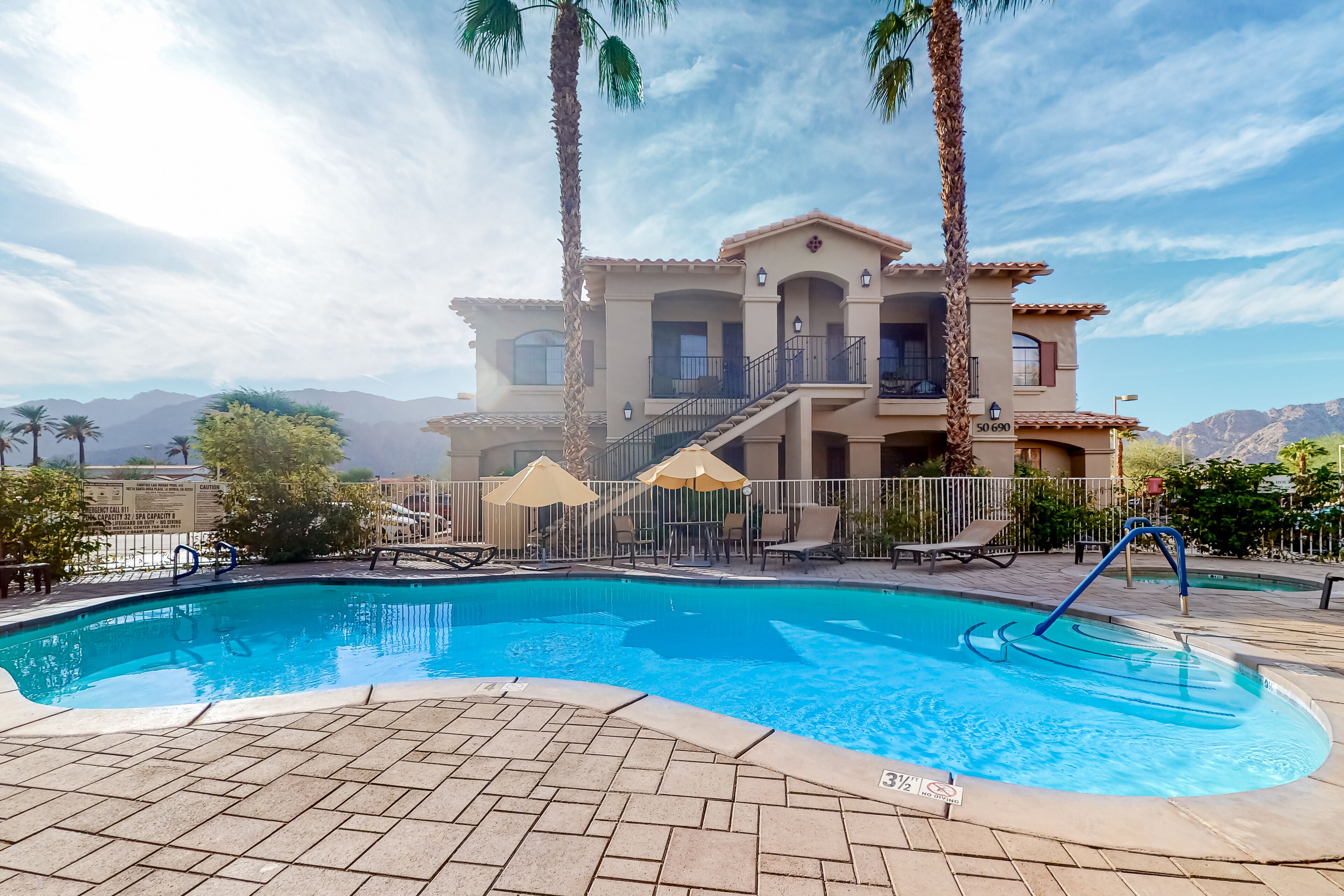 A resort with a swimming pool, palm trees, and a mountain backdrop.