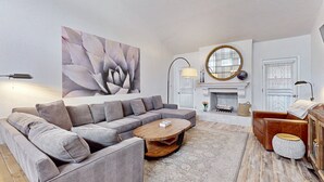 Ein modernes Wohnzimmer mit einem grauen Ecksofa, einem Holztisch und einem runden Spiegel über einem Kamin.