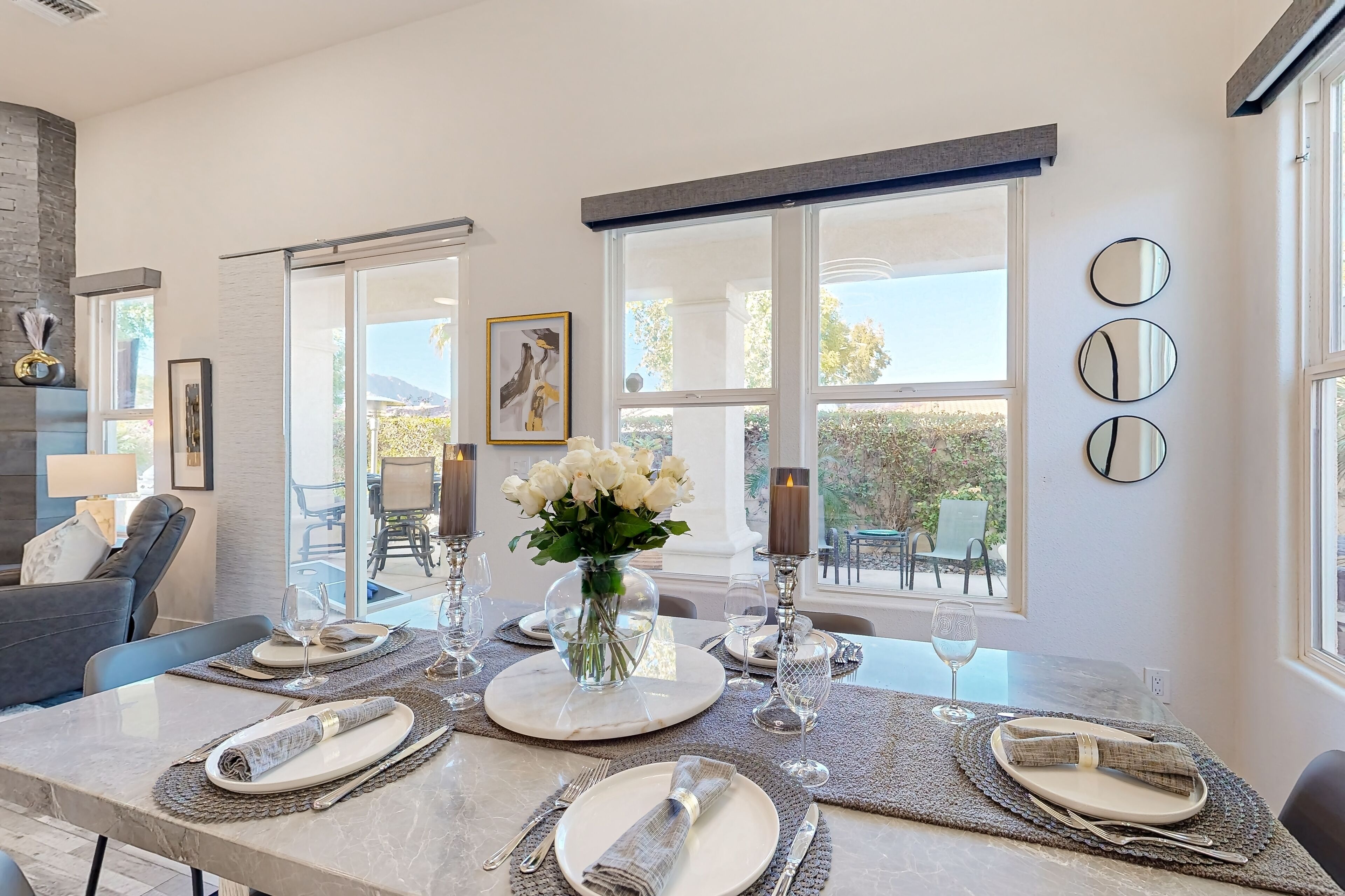 A dining area with a marble table set for four, large windows, and a vase of white flowers.