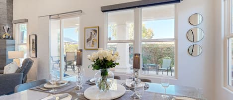 A dining area with a marble table set for four, large windows, and a vase of white flowers.