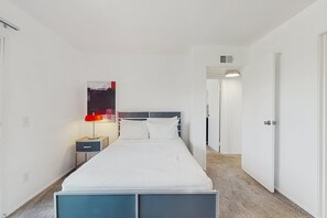 A hotel room with a bed, a nightstand, a lamp, and a door leading to another room. - Mountain View Condo Close to Downtown with Balcony & Shared Pool/Spa/Tennis (Palm Springs)