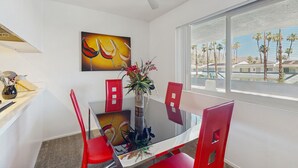 Een moderne eethoek met een glazen tafel, rode stoelen, een vaas met bloemen en een schilderij aan de muur.