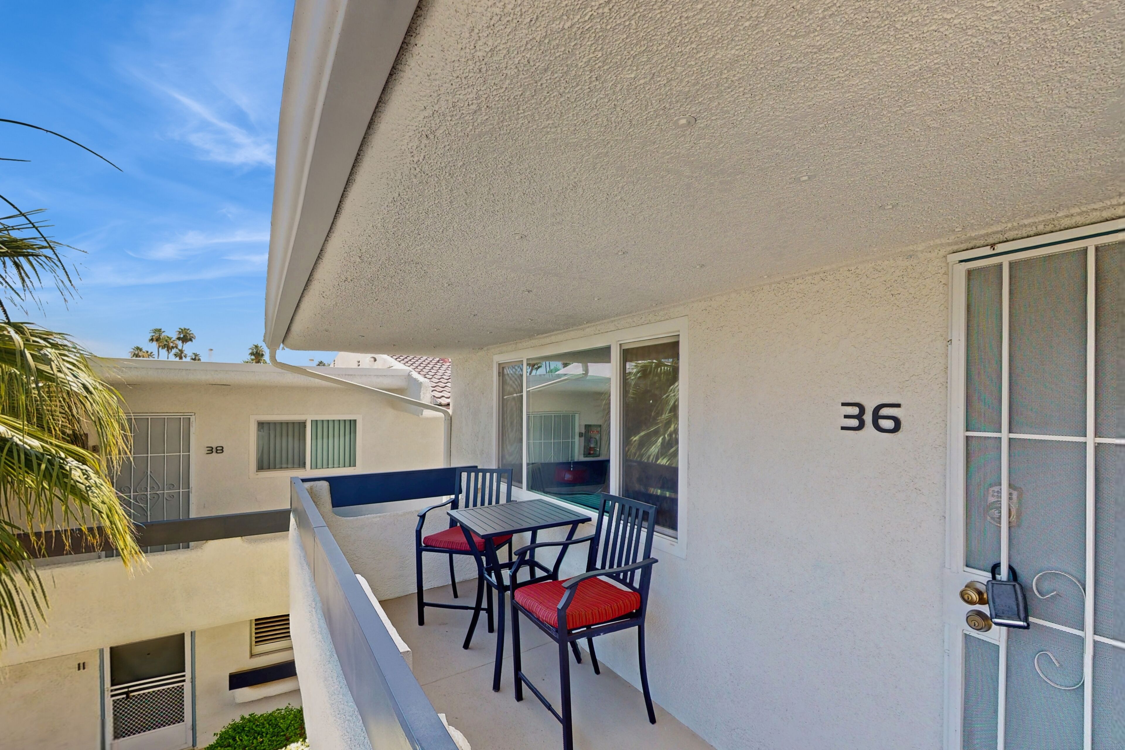 A balcony with a table and chairs, a door with a number, and a view of neighboring buildings.