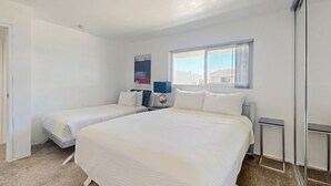 Een hotelkamer met twee enkele bedden, een groot raam met gordijnen, een nachtkastje en een aan de muur hangend kunstwerk.