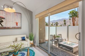 A modern living room with a glass door leading to a balcony with a pool and mountain views. - Colorful home with stunning backyard, pool, spa, WiFi, central AC, and fireplace (Palm Springs)