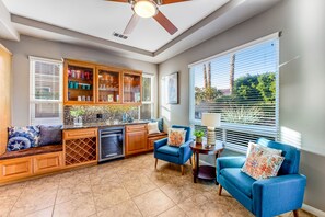 A modern kitchen with a built-in oven, a dining area with a blue sofa, and a large window with blinds. - Dog-friendly desert style home with sprawling pool, pool spa, firepit & grill (La Quinta)