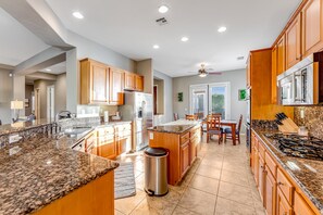 A modern kitchen with granite countertops, wooden cabinets, stainless steel appliances, and a central island. - Dog-friendly desert style home with sprawling pool, pool spa, firepit & grill (La Quinta)