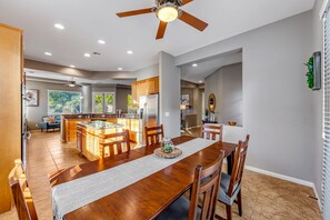 A spacious kitchen with a central island, wooden cabinets, and a dining area with a long table and chairs. - Dog-friendly desert style home with sprawling pool, pool spa, firepit & grill (La Quinta)
