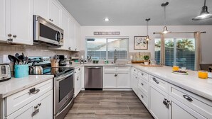 Een moderne keuken met witte kasten, roestvrijstalen apparatuur en een raam met jaloezieën.
