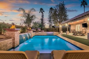 Ein Schwimmbecken mit Wasserfall, umgeben von Liegestühlen und einer Terrasse mit Gartenmöbeln.