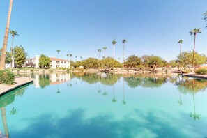 A clear pool surrounded by palm trees and a building with a red roof.