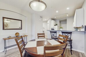Un comedor con una mesa y sillas de madera, un espejo en la pared y una cocina al fondo.