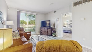 A modern living room with a sofa, armchair, and ottoman, a television, and a sliding glass door leading to a balcony. - Lakefront condo with private washer/dryer, central AC & heated pool (Mesa)